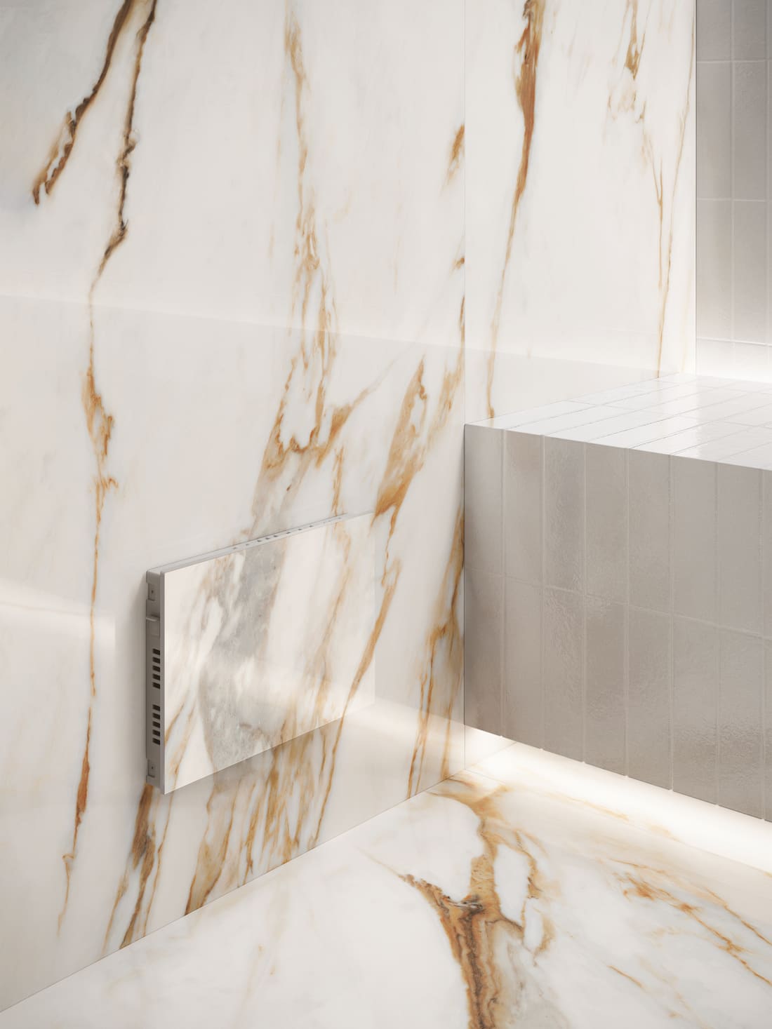 A steam room lined in white marble with gold and grey veining. A slim wall-mounted unit is faced in the same marble with a vent slot along one edge, so it sits almost flush with the wall, beside a tiled bench lit from underneath